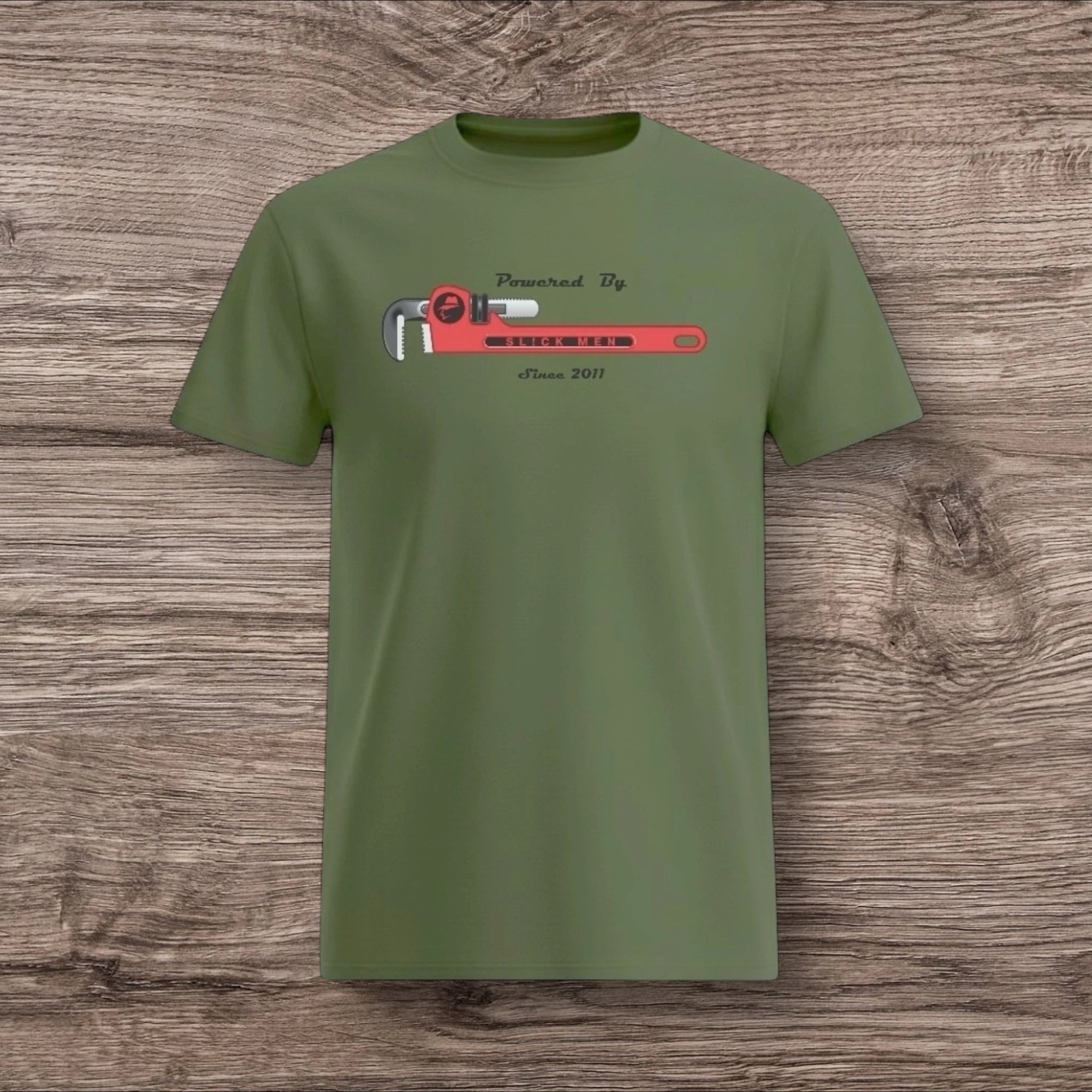 Army green t-shirt with a plumber wrench design on a wooden surface